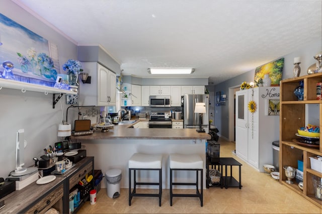 kitchen with a peninsula, white cabinets, appliances with stainless steel finishes, a sink, and dark countertops