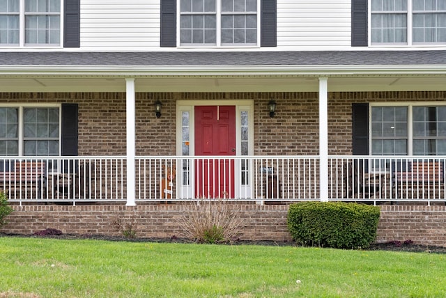 entrance to property featuring a porch, a lawn, and brick siding