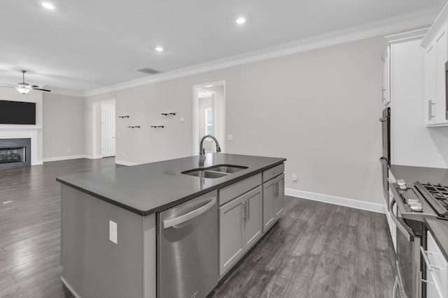 kitchen with a sink, dark countertops, an island with sink, a ceiling fan, and stainless steel appliances