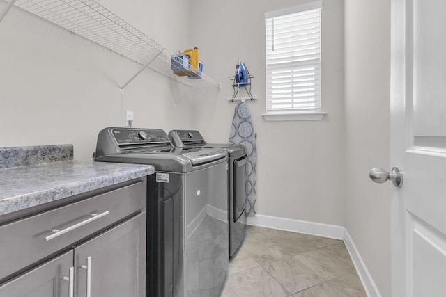 washroom featuring cabinet space, light tile patterned floors, washing machine and clothes dryer, and baseboards