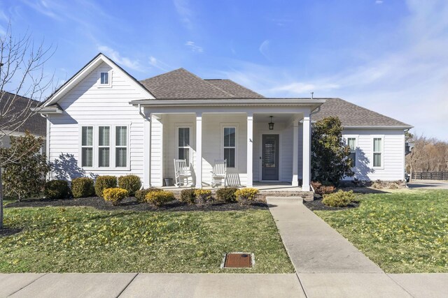 bungalow-style home with a front yard, covered porch, and roof with shingles