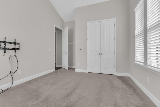 unfurnished bedroom featuring carpet floors, baseboards, a closet, and lofted ceiling