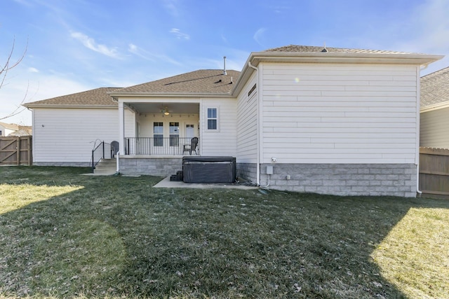 back of property with a patio, roof with shingles, a hot tub, fence, and a lawn