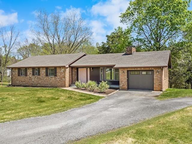 single story home with an attached garage, a chimney, brick siding, a front lawn, and driveway