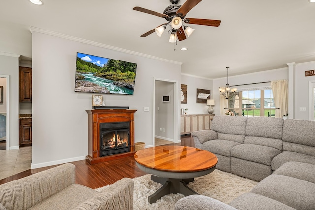 living area with ceiling fan with notable chandelier, ornamental molding, a glass covered fireplace, recessed lighting, and wood finished floors