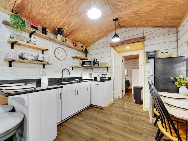 kitchen featuring a sink, dark countertops, lofted ceiling, open shelves, and wooden walls