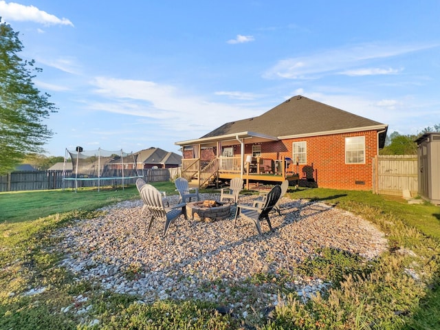 back of property featuring a deck, a lawn, an outdoor fire pit, brick siding, and a trampoline