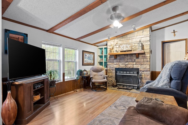 living room with a fireplace, lofted ceiling with beams, a ceiling fan, wood finished floors, and wainscoting