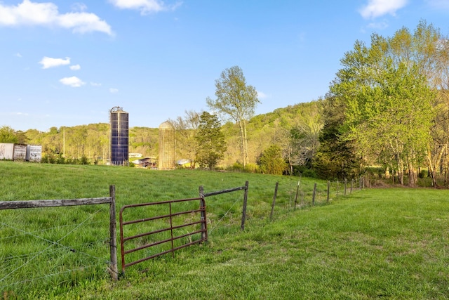view of yard with a rural view, a forest view, and fence