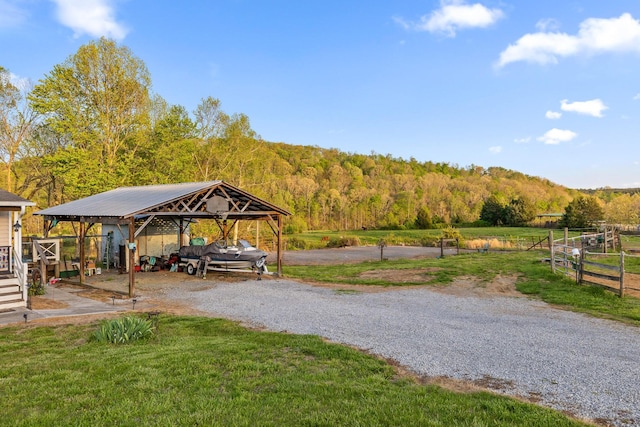 view of home's community featuring a lawn, a detached carport, a view of trees, fence, and driveway