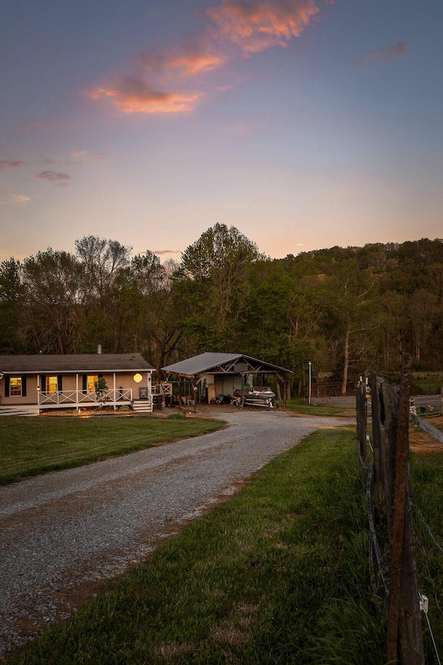 view of front of house with a wooded view, a carport, driveway, and a front yard