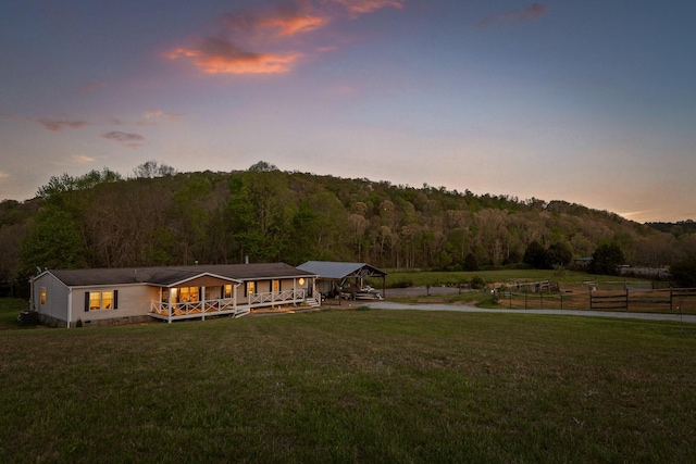 back of property with a yard, a deck, driveway, and a forest view