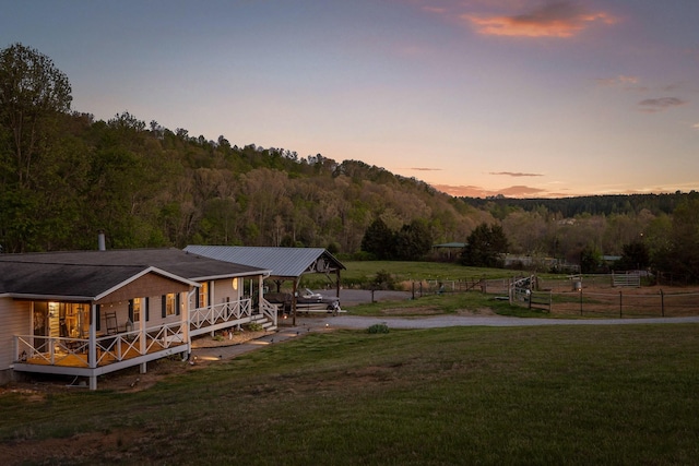 yard at dusk featuring a view of trees, fence, and driveway