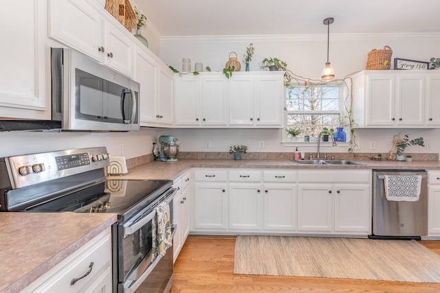 kitchen with crown molding, white cabinets, light countertops, a sink, and stainless steel appliances