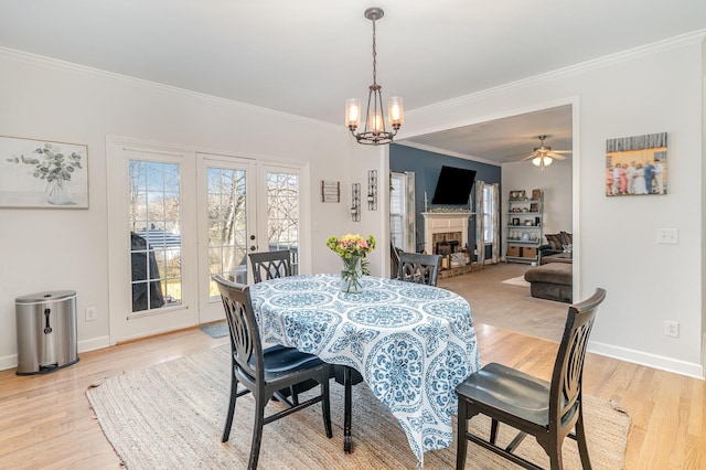 dining space with a fireplace, light wood finished floors, ceiling fan with notable chandelier, and crown molding