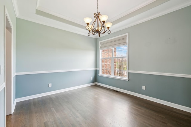 spare room with an inviting chandelier, a tray ceiling, wood finished floors, visible vents, and crown molding