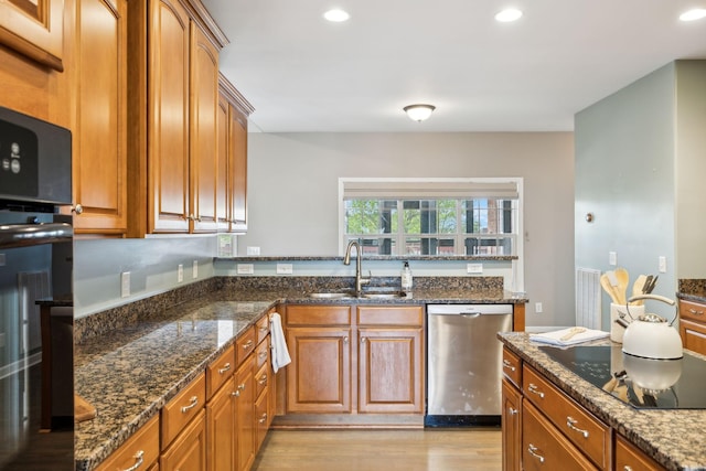 kitchen with brown cabinetry, light wood-style flooring, a sink, and black appliances
