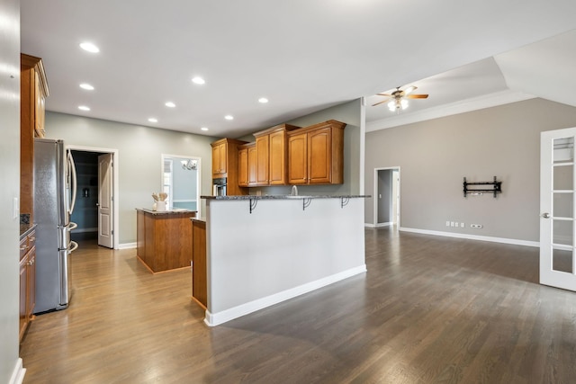 kitchen with a peninsula, freestanding refrigerator, brown cabinets, ceiling fan, and a kitchen island