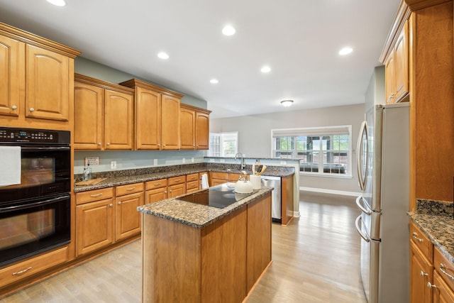 kitchen with black appliances, a peninsula, dark stone countertops, and light wood-style floors