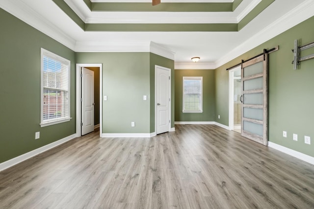 unfurnished bedroom with crown molding, light wood-style floors, a raised ceiling, and a barn door