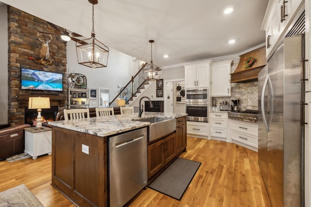 kitchen with white cabinets, a sink, a stone fireplace, appliances with stainless steel finishes, and backsplash