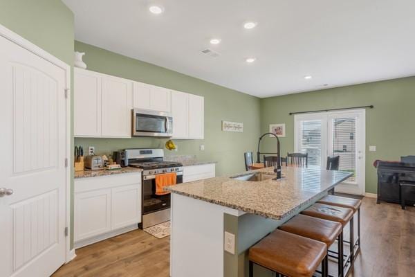 kitchen featuring a kitchen breakfast bar, a sink, white cabinetry, appliances with stainless steel finishes, and light stone countertops
