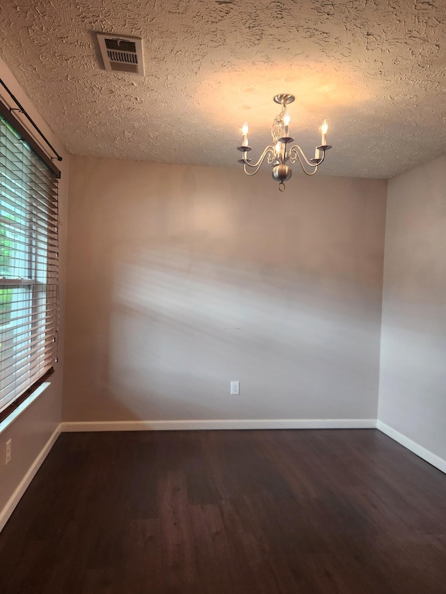 unfurnished room featuring an inviting chandelier, a textured ceiling, visible vents, dark wood-style flooring, and baseboards