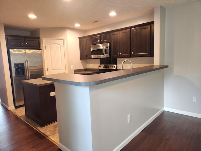 kitchen with dark brown cabinetry, a peninsula, stainless steel appliances, and wood finished floors