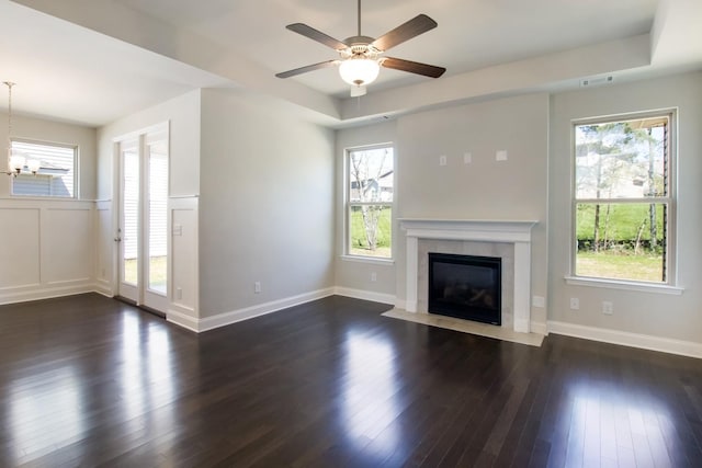 unfurnished living room featuring a wainscoted wall, dark wood-type flooring, visible vents, a high end fireplace, and ceiling fan with notable chandelier