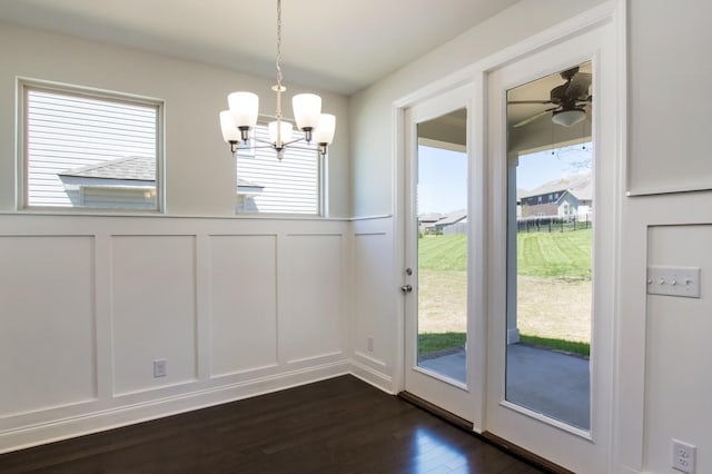 doorway to outside with a decorative wall, dark wood-style floors, ceiling fan with notable chandelier, and a wainscoted wall