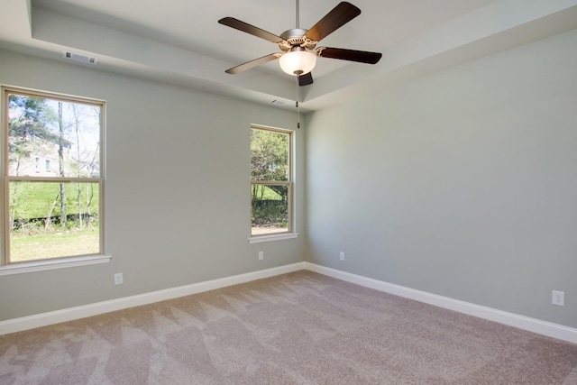 spare room with a raised ceiling, light colored carpet, visible vents, and plenty of natural light