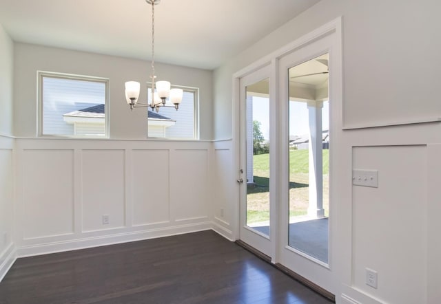 unfurnished dining area with dark wood-type flooring, a decorative wall, an inviting chandelier, and a wainscoted wall
