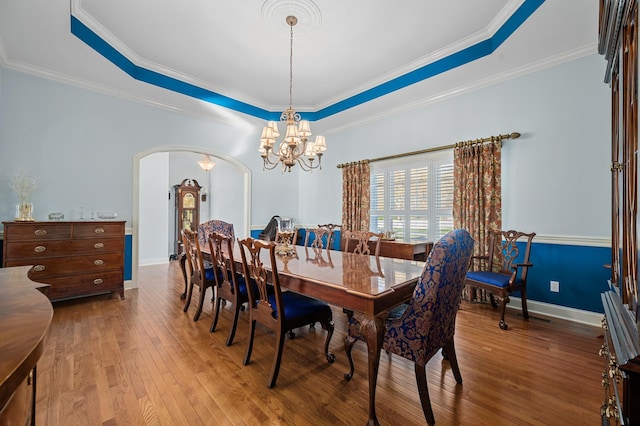 dining room with wood-type flooring, a raised ceiling, arched walkways, and an inviting chandelier