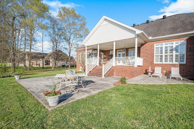 rear view of property featuring brick siding, a patio, a yard, and covered porch