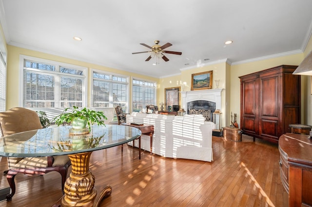 living area featuring a glass covered fireplace, hardwood / wood-style floors, ornamental molding, and ceiling fan