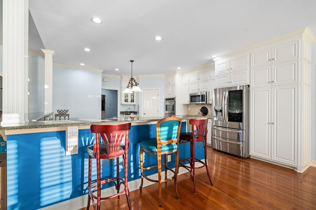 kitchen with a peninsula, white cabinetry, dark wood-type flooring, a breakfast bar area, and appliances with stainless steel finishes