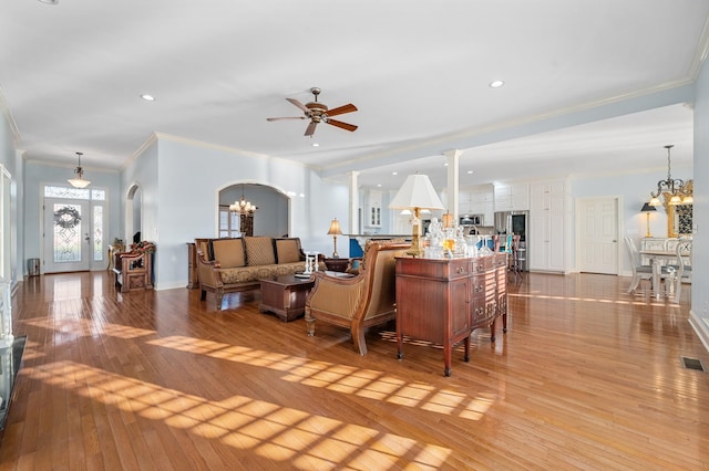 living room featuring crown molding, ceiling fan with notable chandelier, arched walkways, light wood finished floors, and baseboards
