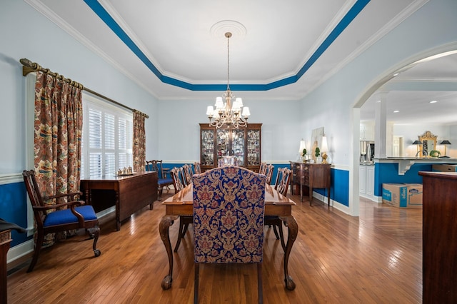 dining area with wood-type flooring, a tray ceiling, arched walkways, and a chandelier