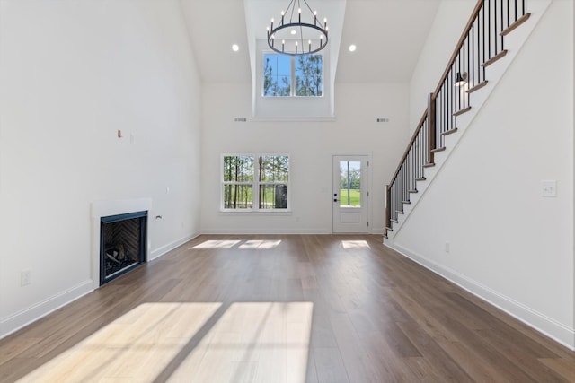 unfurnished living room with a towering ceiling, a chandelier, a fireplace, stairway, and wood finished floors