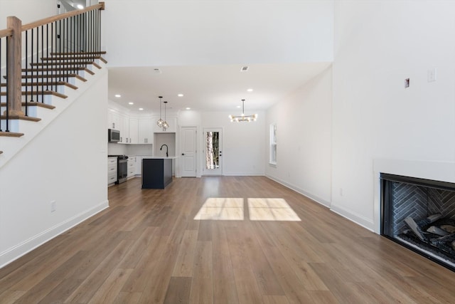 unfurnished living room featuring baseboards, an inviting chandelier, a sink, light wood finished floors, and stairway
