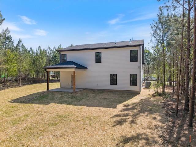 rear view of house with an attached carport, a patio, central AC, and a lawn