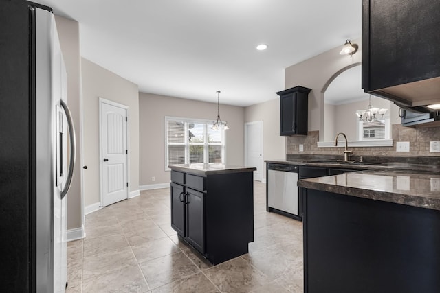 kitchen featuring dark cabinets, appliances with stainless steel finishes, a notable chandelier, decorative backsplash, and a sink