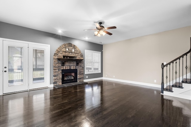 unfurnished living room featuring baseboards, ceiling fan, a fireplace, wood finished floors, and stairs