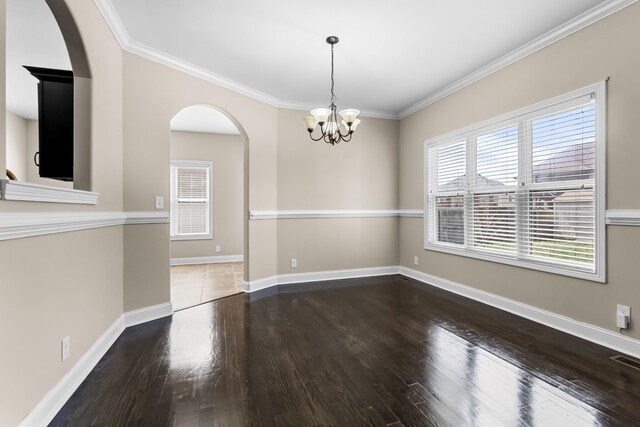spare room with arched walkways, ornamental molding, a chandelier, wood finished floors, and baseboards