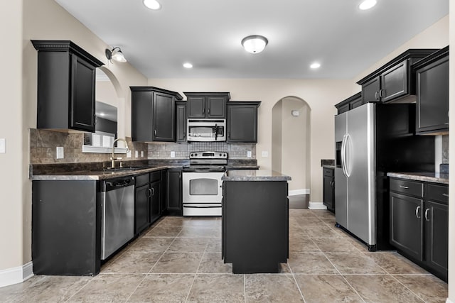 kitchen with dark cabinets, arched walkways, a center island, a sink, and stainless steel appliances