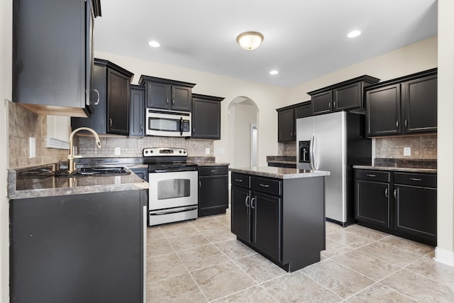 kitchen featuring tasteful backsplash, dark cabinetry, stainless steel appliances, arched walkways, and a sink
