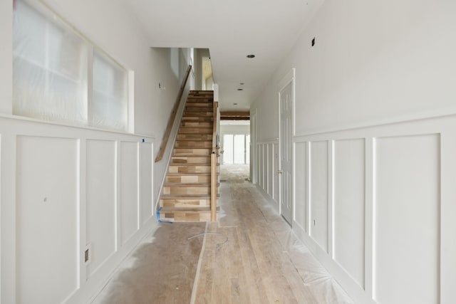 corridor with a decorative wall, stairway, light wood-type flooring, and a wainscoted wall
