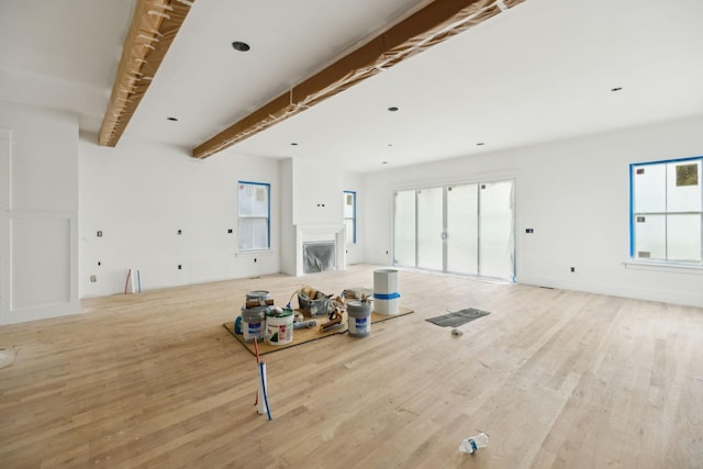 unfurnished living room with light wood-style flooring, a fireplace, and beam ceiling