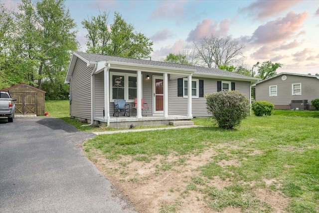 single story home with a storage shed, a front lawn, a porch, an outbuilding, and cooling unit