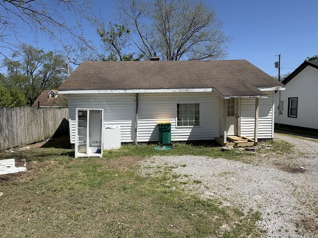 back of property with a yard, roof with shingles, entry steps, and fence